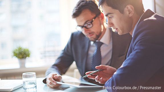 Zwei Männer im Büro sehen gemeinsam auf Tablet und besprechen sich