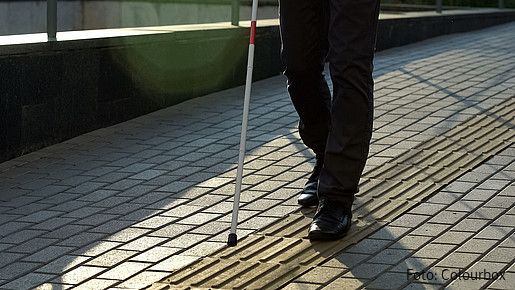 Foto zum Thema Blindheit und Leben mit einer Sehbehinderung: Zu sehen ist eine blinde Person, die sich mit einem Blindenstock an einem Leitsystem orientiert.