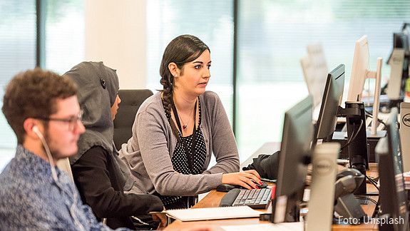 Blick in ein Büro auf einen jungen Mann und zwei Frauen, eine von ihnen trägt ein Kopftuch. Alle schauen auf ihre Computer-Bildschirme