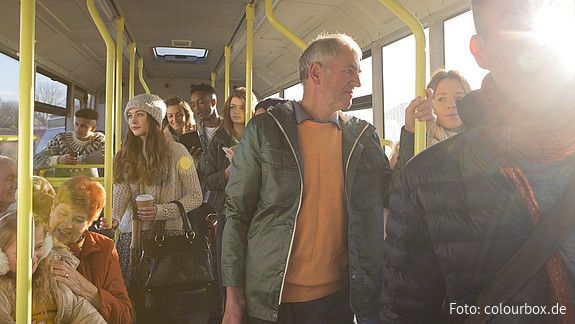 Blick in den Innenraum eines Busses auf stehende und sitzende Passagiere aus allen Altersgruppen